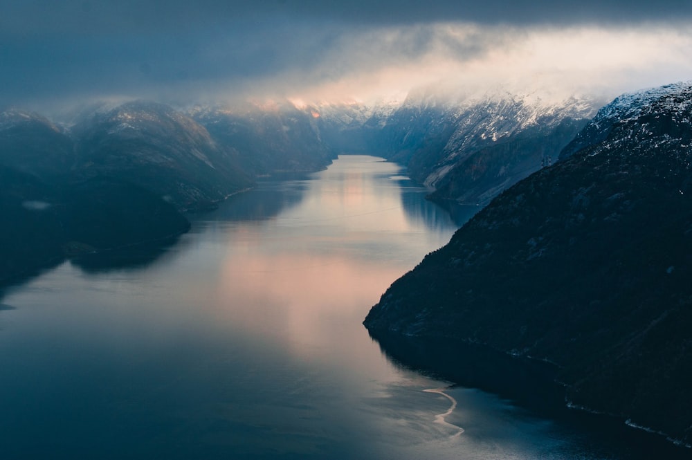 a body of water surrounded by mountains under a cloudy sky