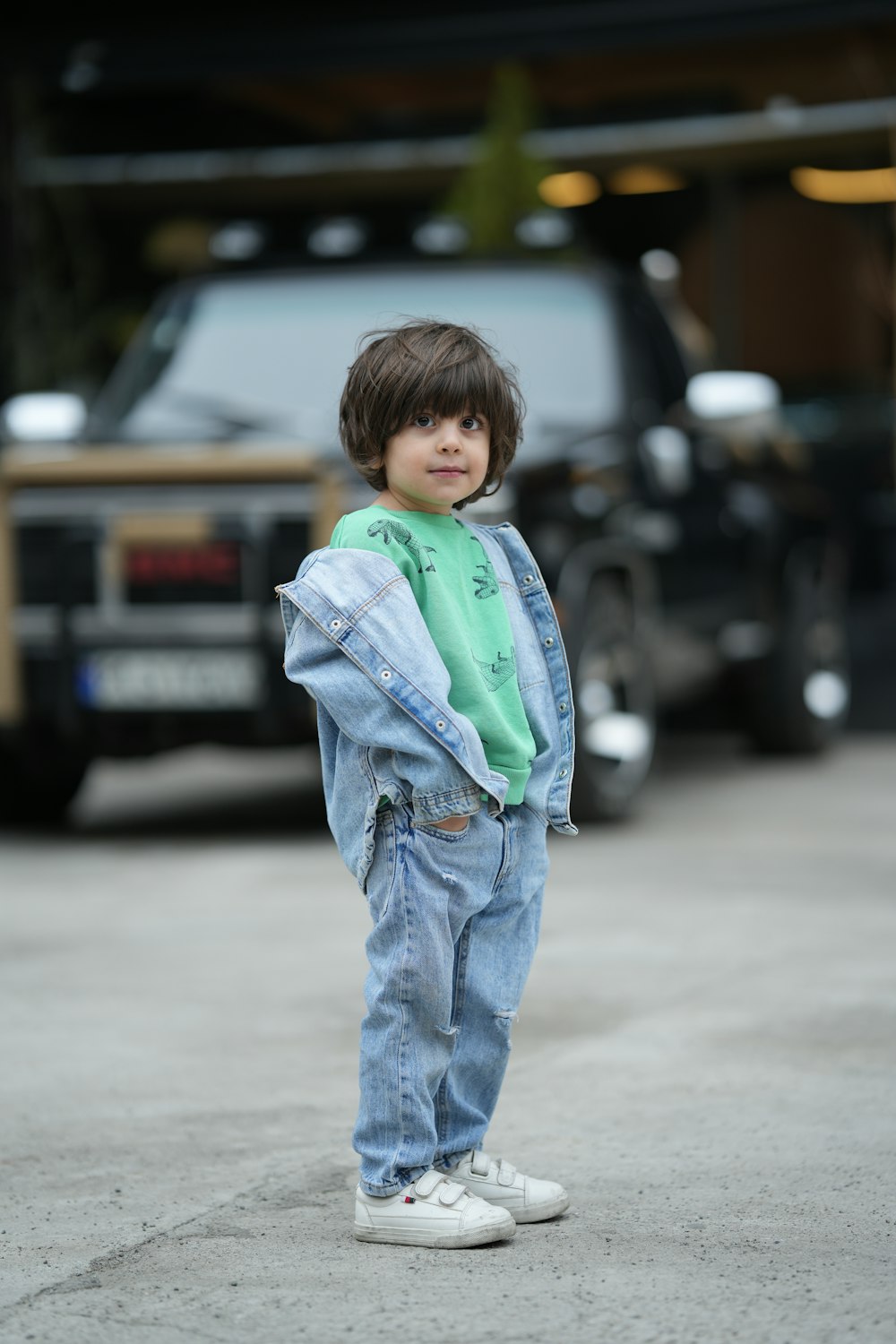 a young boy standing on a sidewalk in front of a truck