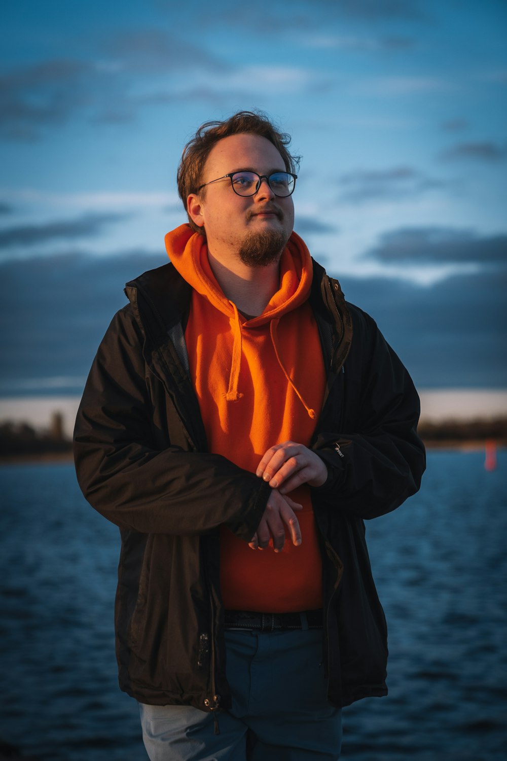 a man with a beard and glasses standing by the water