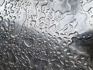 Sterile water droplets forming on a smooth metallic surface, reflecting turquoise and silver hues.