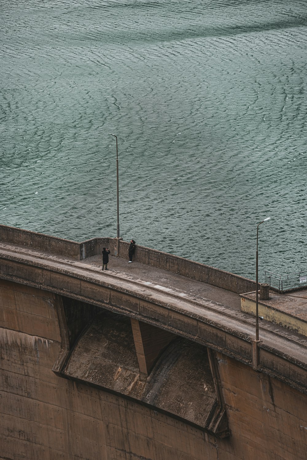 two people standing on a bridge over looking the water