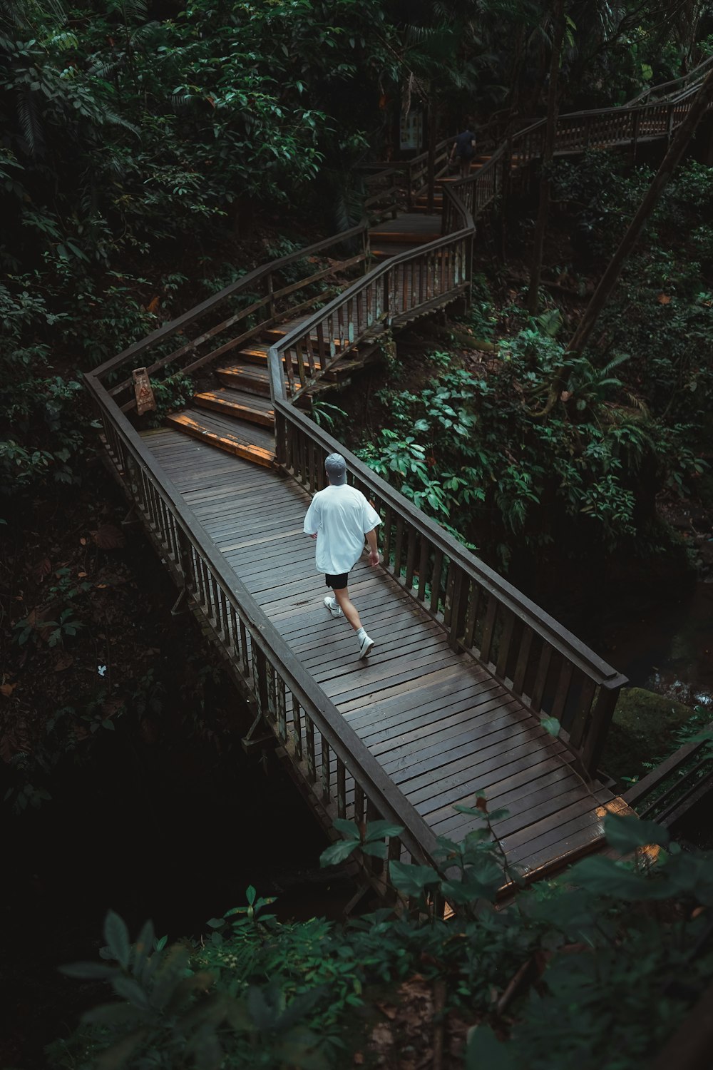 a man walking across a wooden bridge in the woods