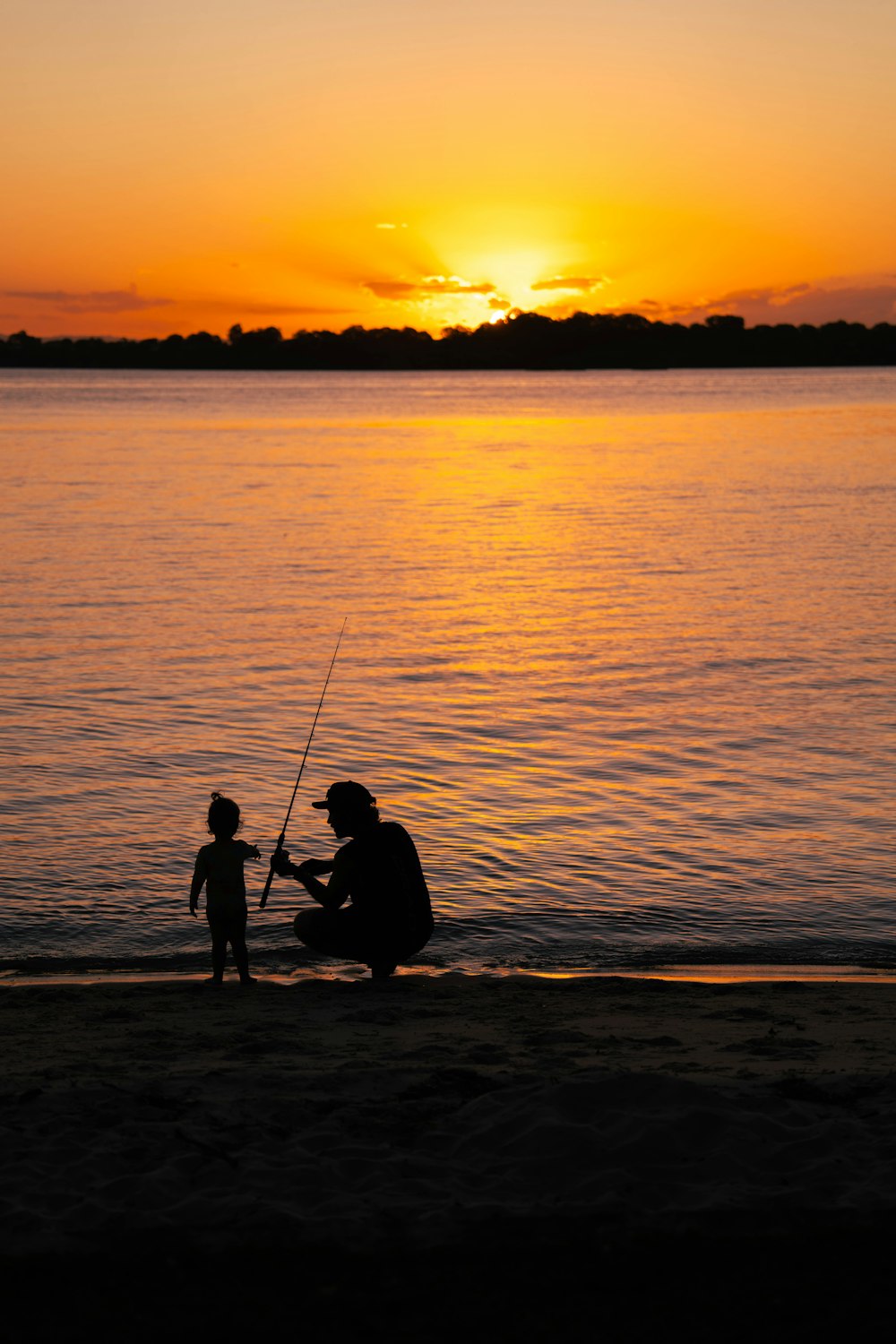 a father and son fishing on the beach at sunset