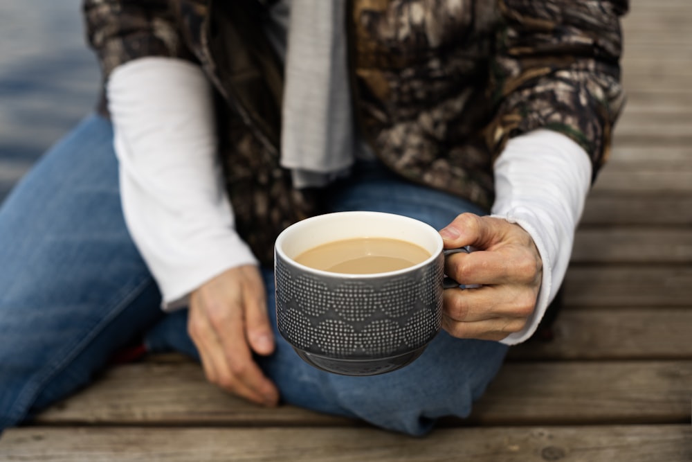 a man sitting on a dock holding a cup of coffee