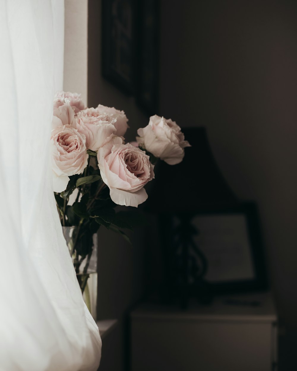 a vase filled with pink roses sitting next to a window