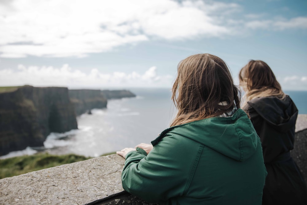 a couple of women sitting on top of a cliff