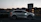 Tow truck loading a sleek SUV on a platform at dusk near busy city streets.