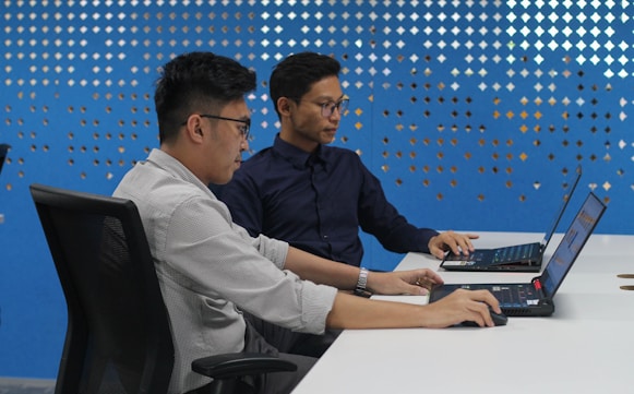 two men sitting at a table with laptops