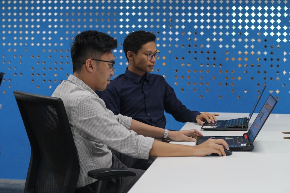 two men sitting at a table with laptops