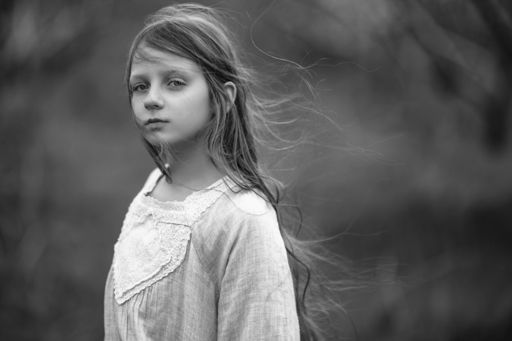 a young girl with long hair standing in front of a tree