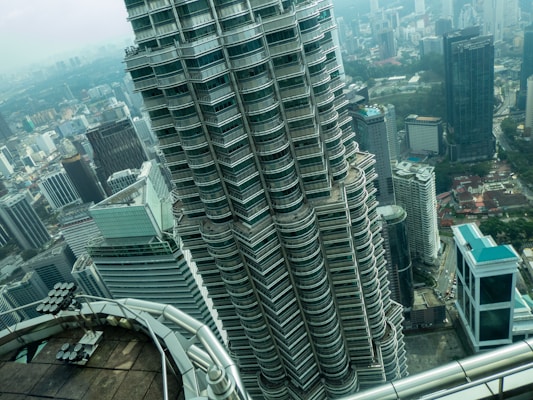 A high-rise skyscraper with a distinct architectural design featuring multiple tiers of rounded edges. The urban skyline in the background includes several other tall buildings and a sprawling cityscape. The view suggests a perspective from another skyscraper nearby.