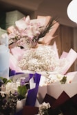 A collection of beautifully arranged flower bouquets featuring a variety of flowers including lilies, roses, and baby's breath. The bouquets are wrapped in colorful paper such as pink, purple, and white, and are placed against a softly lit background.
