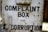 A rusty metal box with the words 'Complaint Box for Corruption' written in bold black letters. The surface is weathered and shows signs of age with patches of rust and dirt.
