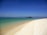 A serene beach view in Djerba with soft waves and golden sand under a clear blue sky.