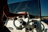Close-up of a hand steering a wooden boat wheel over sparkling ocean water.