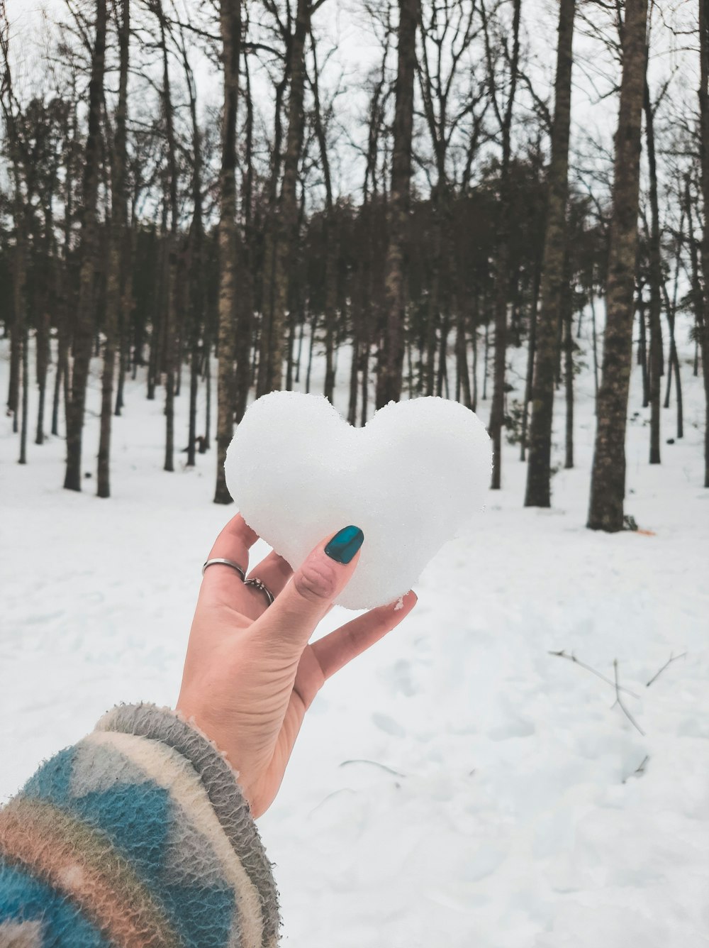 une personne tenant une boule de neige en forme de cœur dans la neige