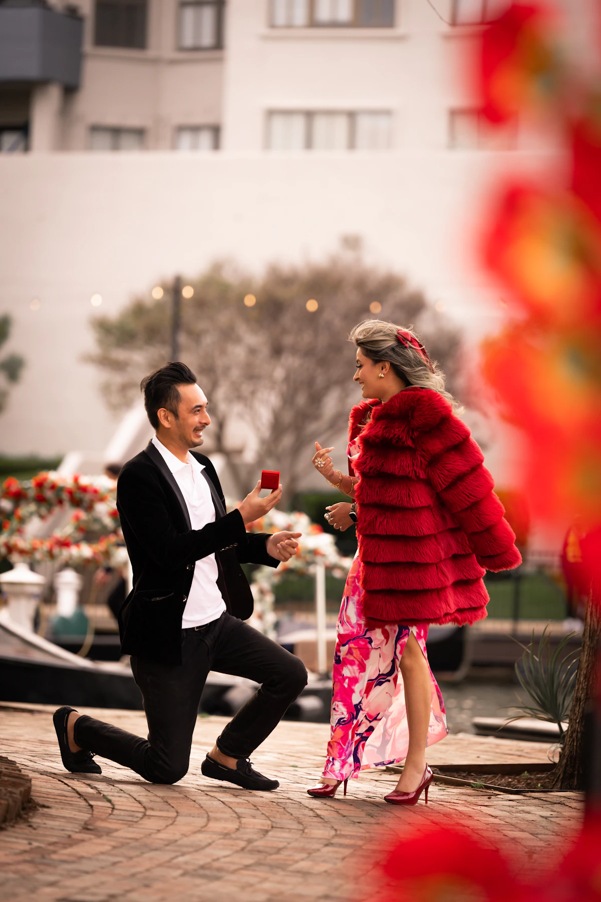 A man kneeling beside a woman holding a rose in a proposal scene