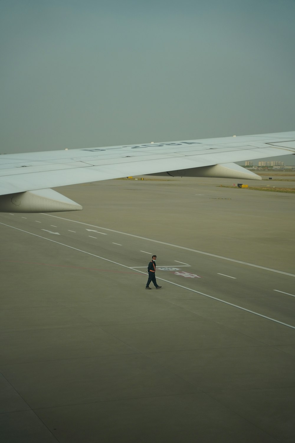 a man walking across an airport tarmac next to an airplane wing