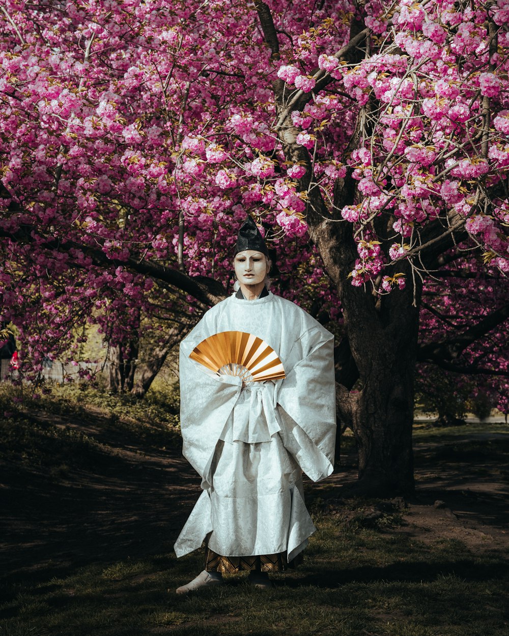 a woman in a kimono standing in front of a tree with pink flowers