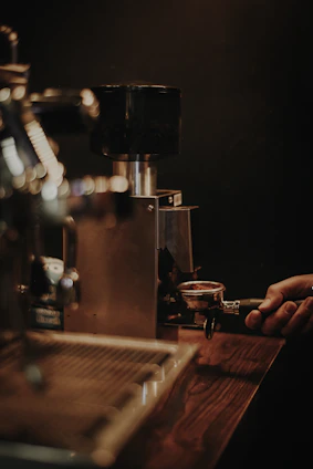 A close-up of hands expertly grinding fresh coffee beans next to a camera setup capturing the process.
