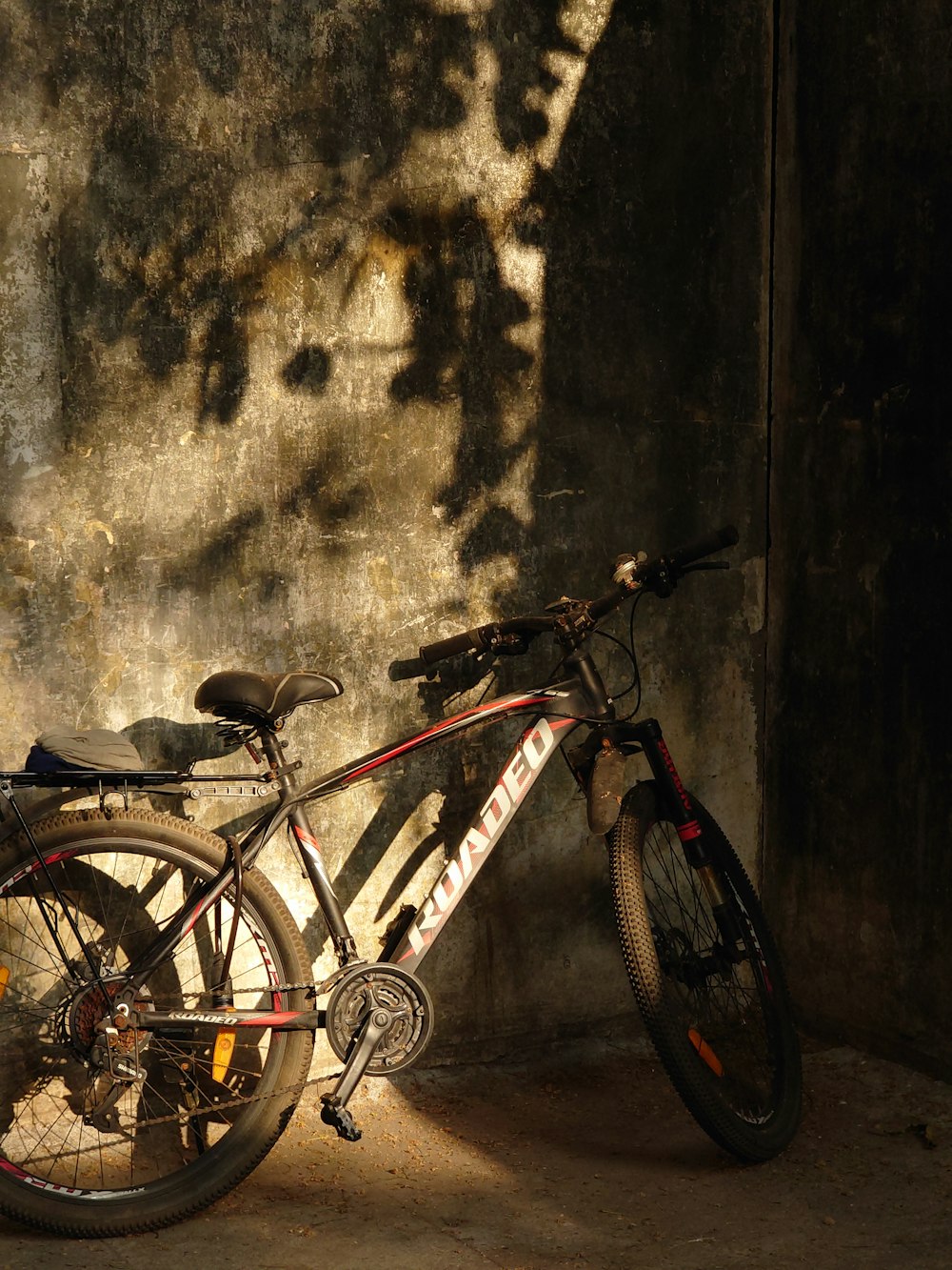 Una bicicleta apoyada contra una pared a la sombra