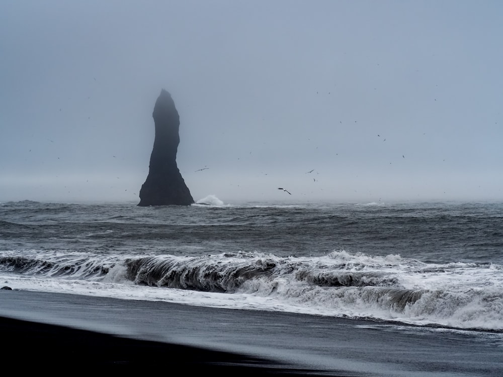 a large rock sticking out of the ocean on a foggy day