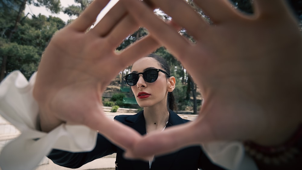 a woman wearing sunglasses making a heart shape with her hands