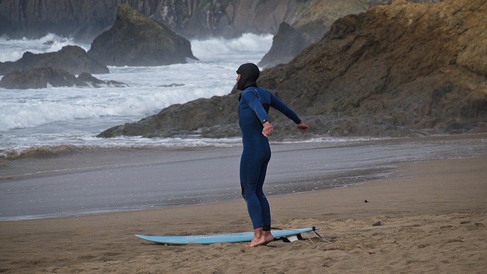 a woman in a wetsuit standing on a surfboard on the beach