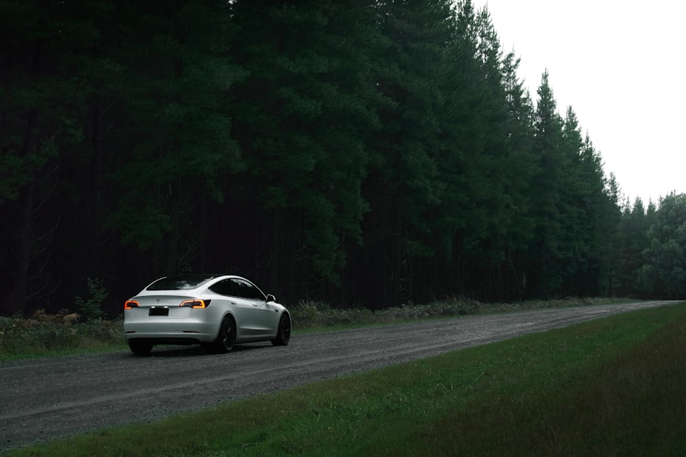 a white car driving down a road next to a forest