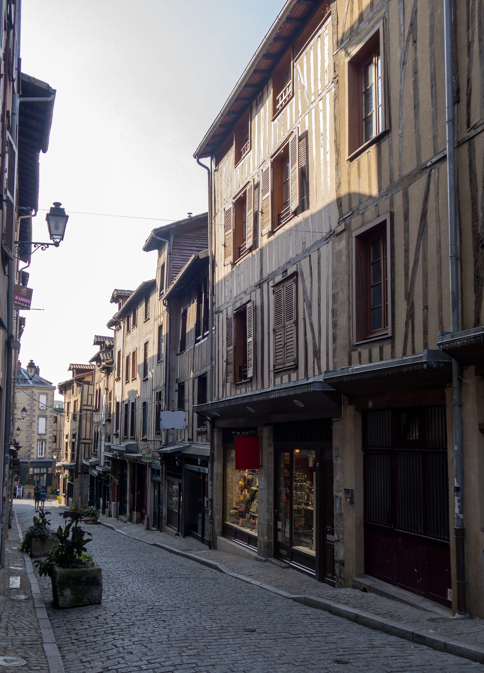 A quiet cobblestone street in an old European town, lined with weathered stone buildings and warm window glows.