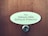 A wooden door features an oval nameplate with black text displaying names, and a metal doorbell or peephole is situated below it.