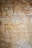 Ancient Egyptian hieroglyphs and relief carvings on a stone wall featuring figures with headdresses, symbols, and detailed attire. The artwork includes registers filled with various intricate symbols in subtle hues.
