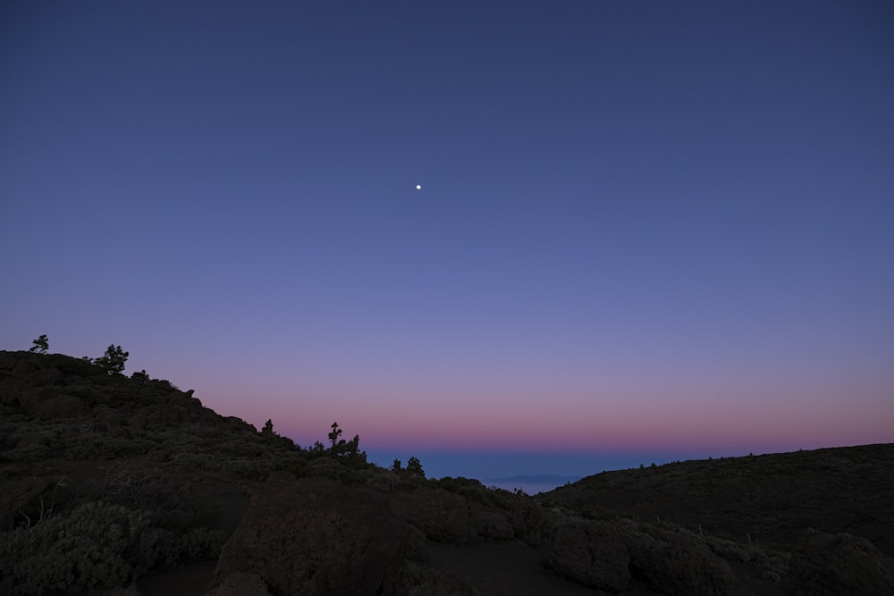 the moon is setting over a rocky hill