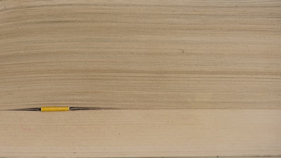 A close-up view of the edge of a thick book, showing many layers of aged, yellowing paper. A slim, yellow pencil is partly visible between the pages, highlighting the macro perspective of the image.