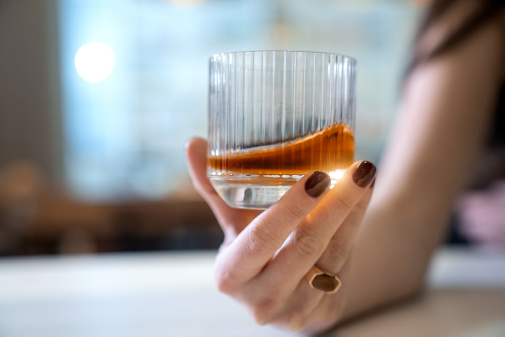 a woman holding a glass with a liquid inside of it