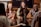 A group of four friends are sitting around a polished wooden table, laughing and enjoying drinks in a cozy, stylish setting. The group appears to be engaged in a warm and lively conversation, creating an atmosphere of camaraderie and joy.