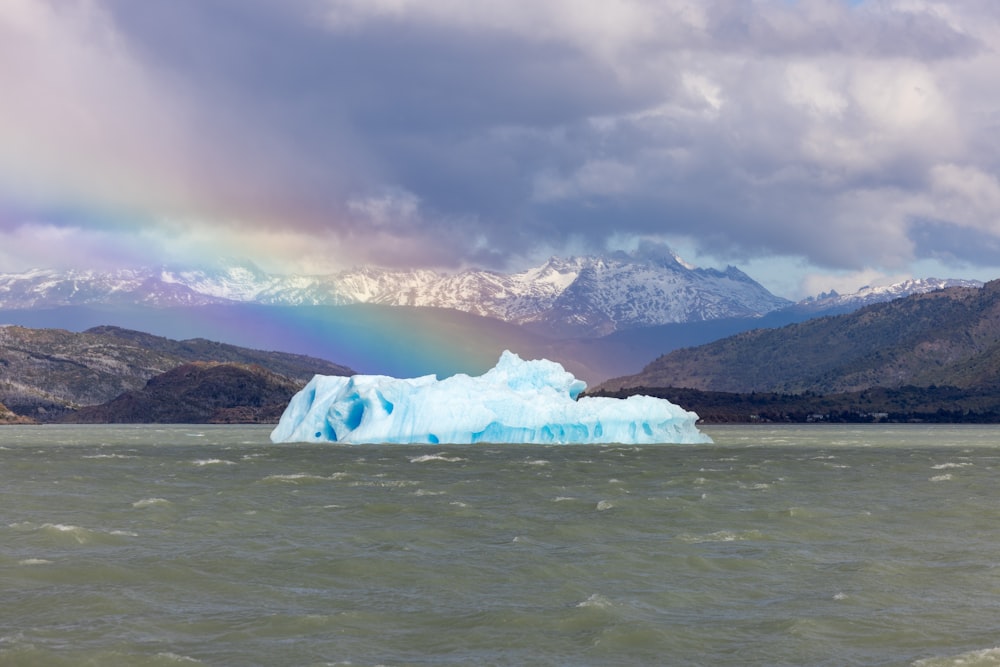 a large iceberg floating on top of a lake under a rainbow
