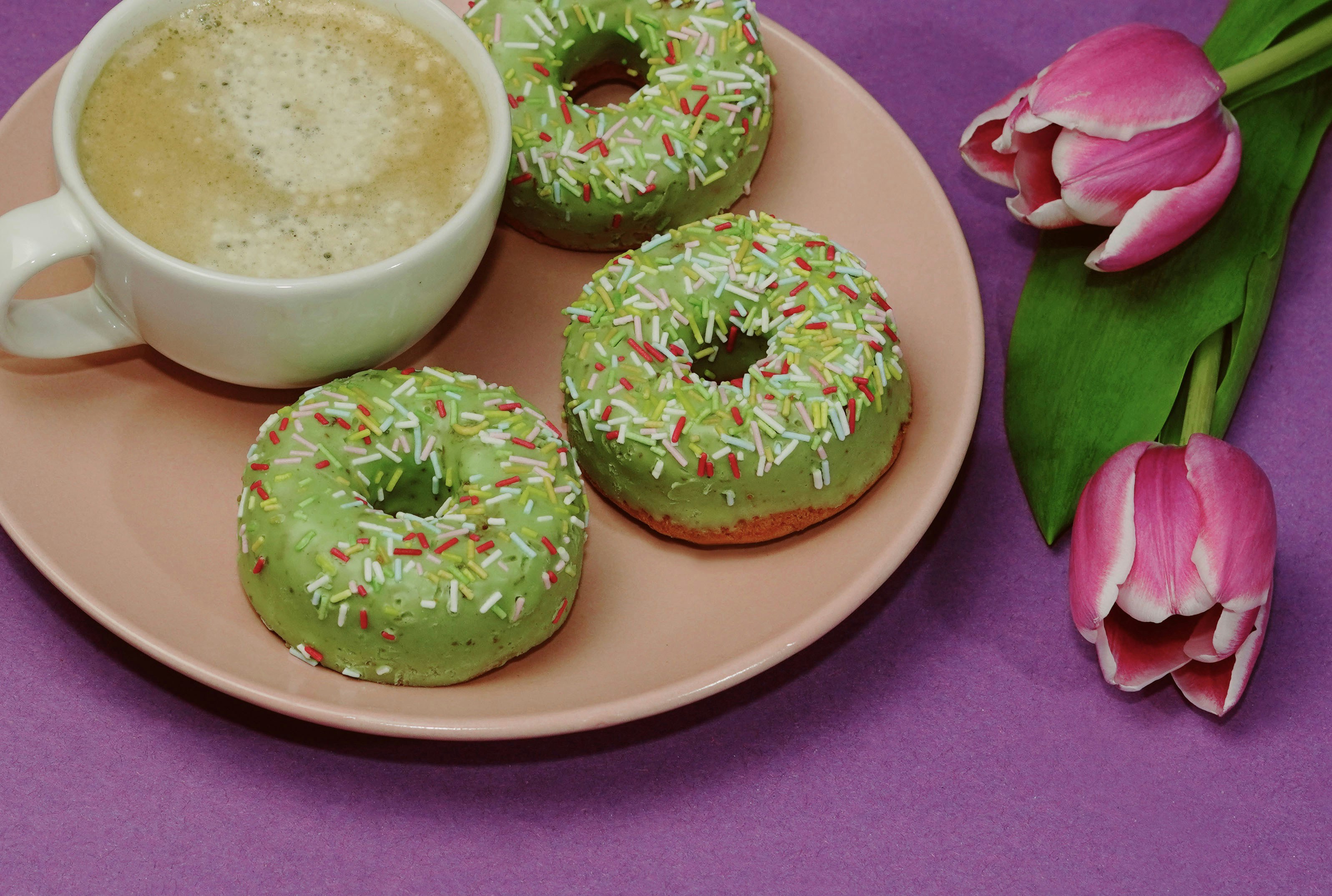 a pink plate topped with donuts and a cup of coffee
