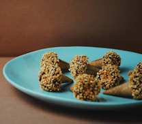 Several small ice cream cones, each topped with a round scoop coated in crushed nuts, arranged in a circular pattern on a blue plate. The background is a plain, brown surface, creating a simple and elegant presentation.
