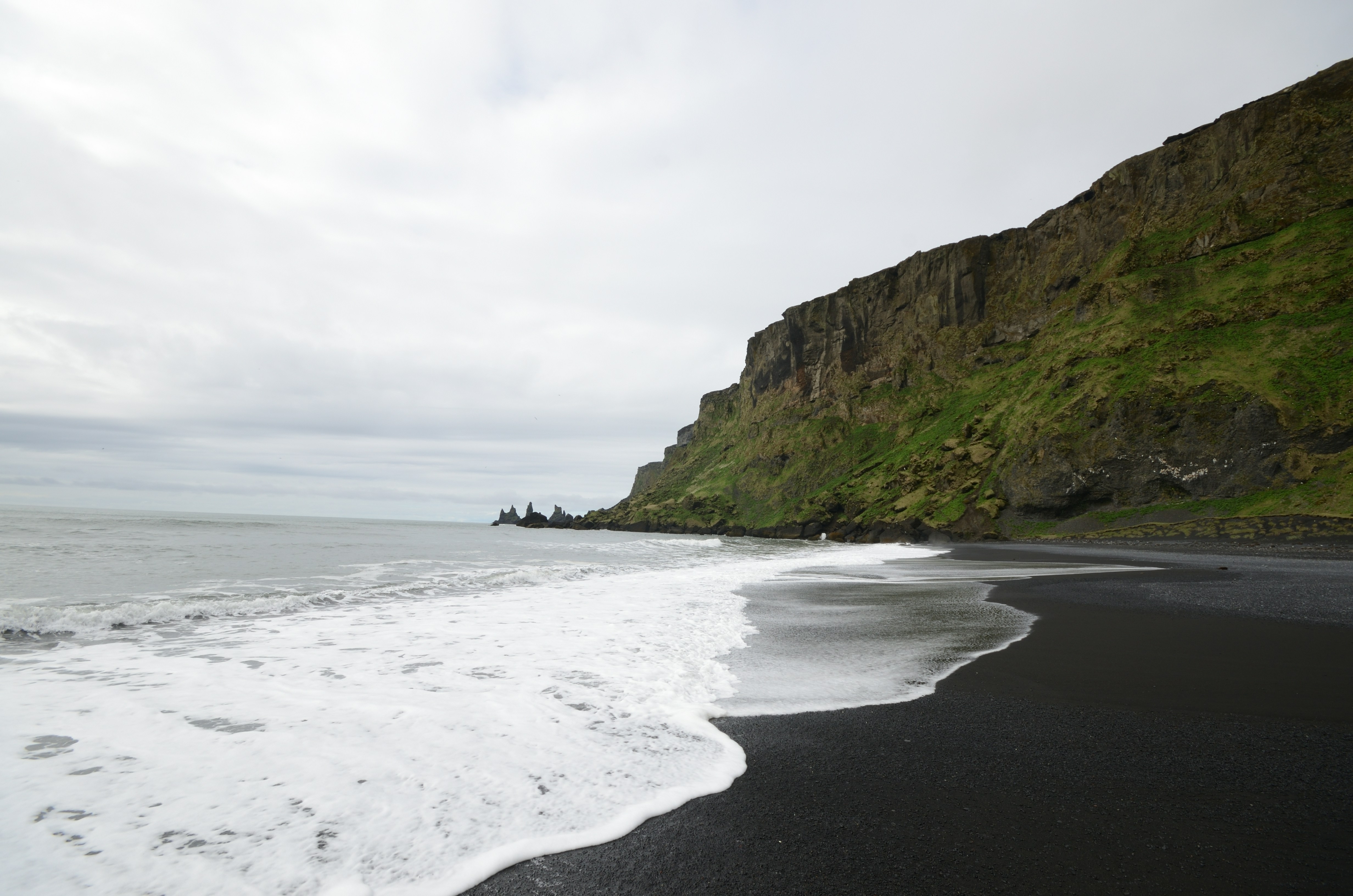 a black sand beach with a cliff in the background, 