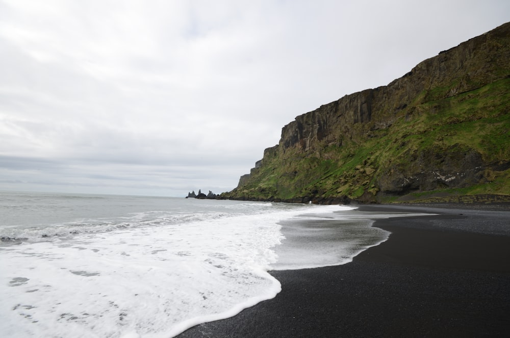 a black sand beach with a cliff in the background