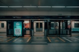 An empty subway platform features illuminated advertising, with a QR code visible in the center. Subway doors are open, revealing the interior seating area. The signage above the platform indicates directions and locations in a transport system.
