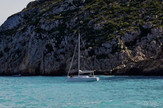 Boat sailing near turquoise waters with rocky cliffs in the background under a sunny sky.