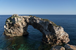 A bright, sunny photo capturing the natural limestone arch of Durdle Door with clear blue skies and turquoise sea.