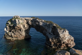 A bright, sunny photo capturing the natural limestone arch of Durdle Door with clear blue skies and turquoise sea.