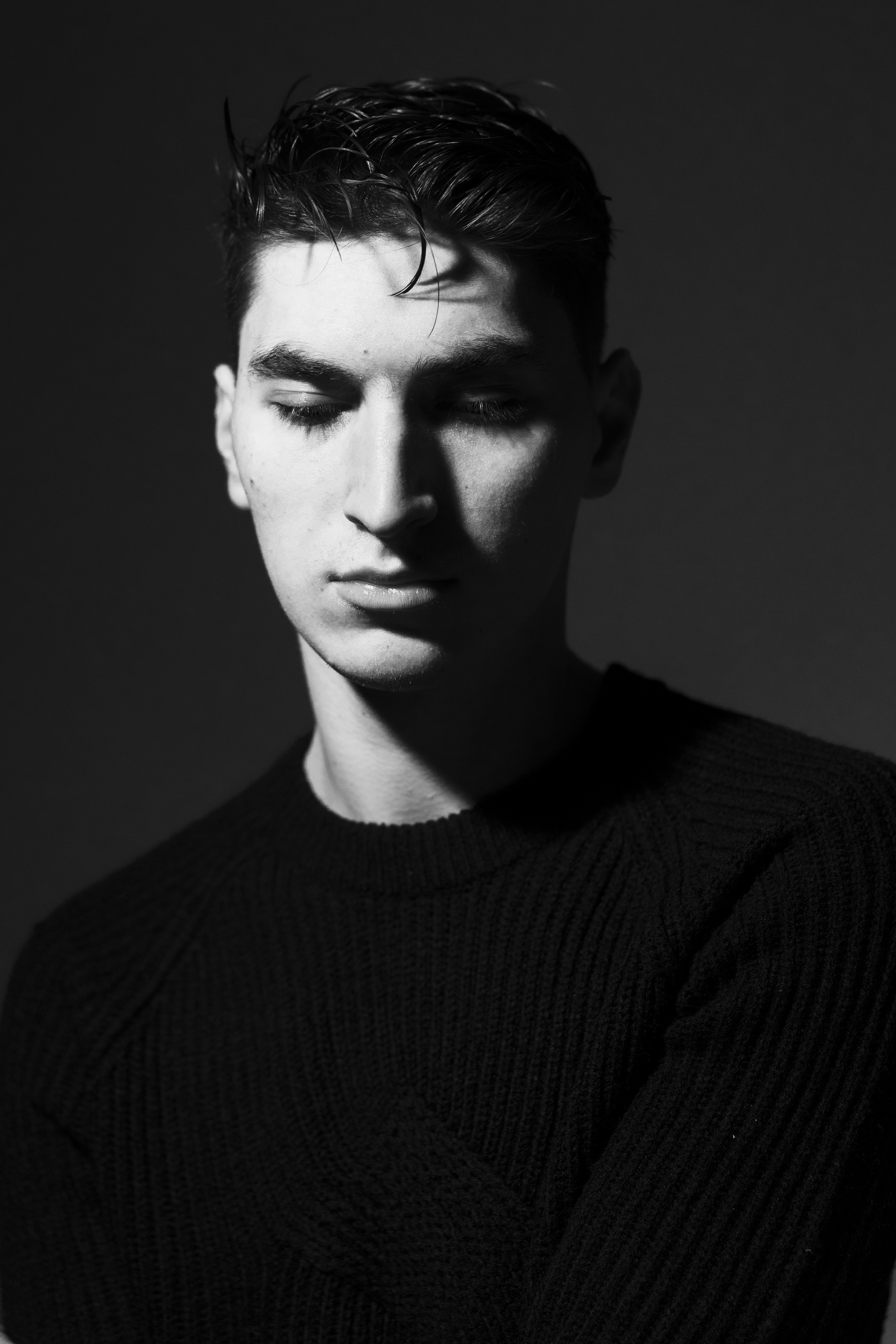 a young man in a black sweater poses for a black and white photo