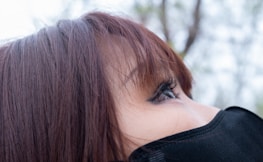 Close-up of a person's face focusing on the eye area, with eyelashes prominent and hair partially covering the forehead. The person is wearing a black face mask.