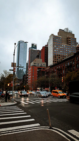 An old Manhattan street scene in the late seventies under a cloudy sky, busy with taxis and pedestrians.