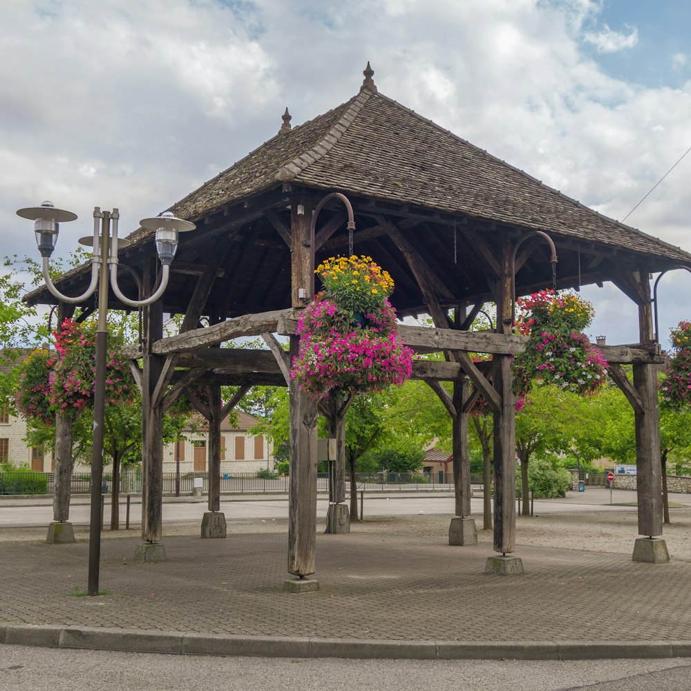 a wooden gazebo with flowers hanging from it's roof