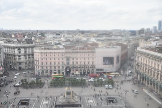 Wide-angle panoramic shot from the camera showing a bustling public square with multiple people and vehicles.